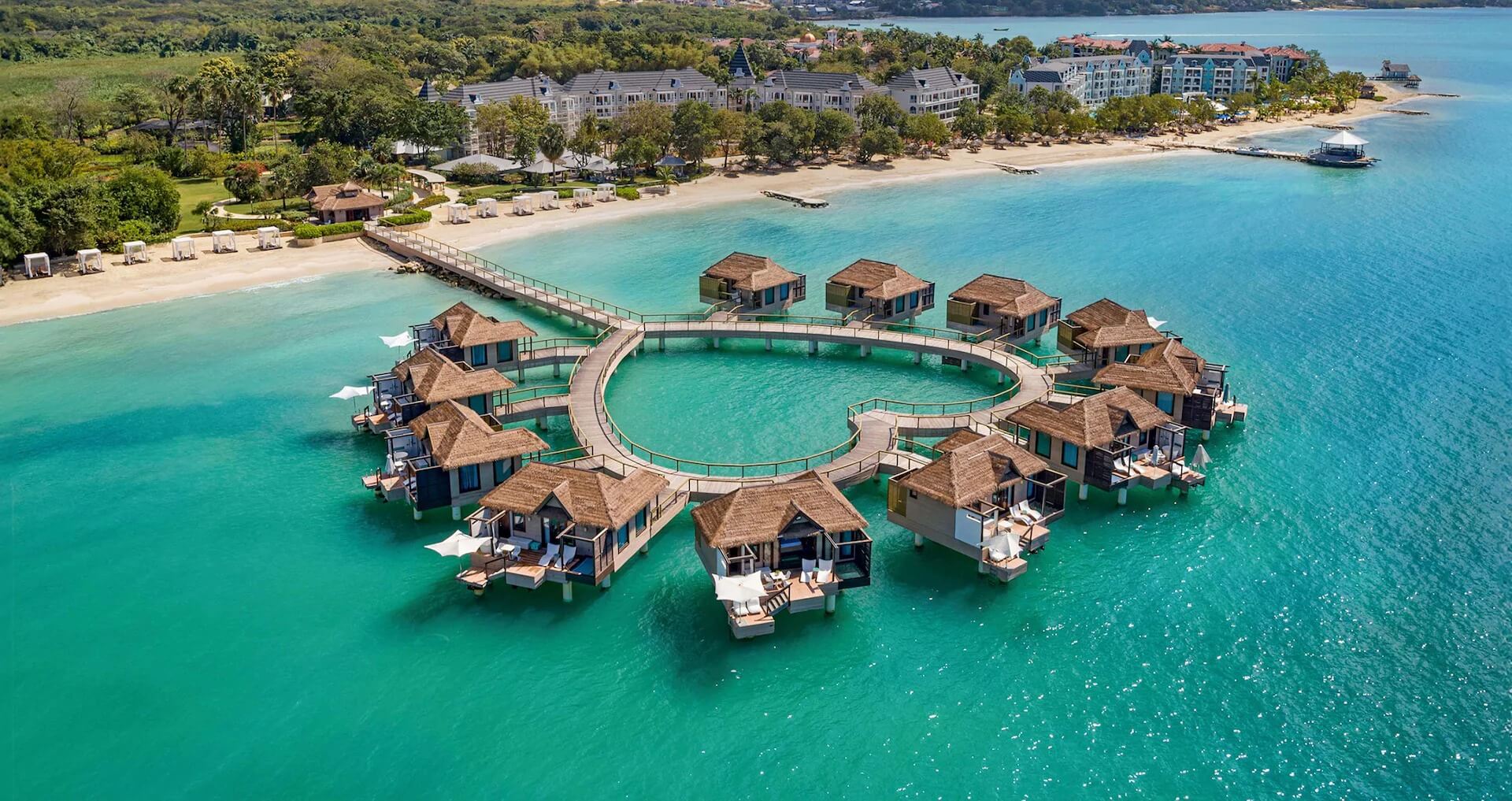Aerial view of over-the-water villas circling turquoise Caribbean water at a Sandals resort