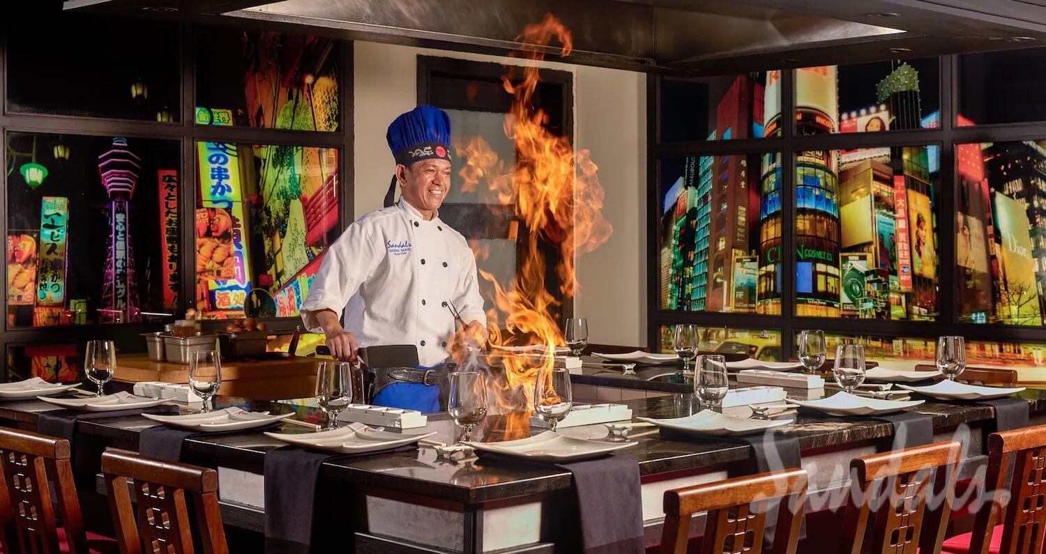 Hibachi chef cooking over flames at a teppanyaki table set for dinner at a Sandals restaurant